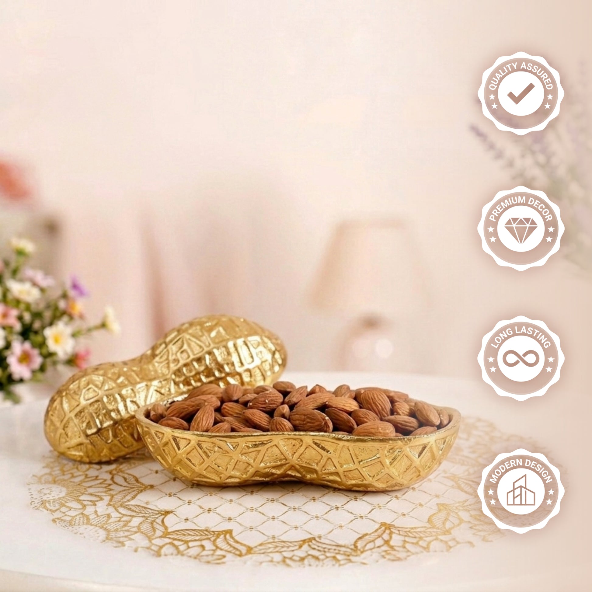 A decorative gold serving bowl shaped like a peanut shell, filled with raw almonds. The matching textured gold lid rests beside it on a white table adorned with a gold lace doily. The background is softly blurred, showing hints of floral arrangements and a warm lamp.