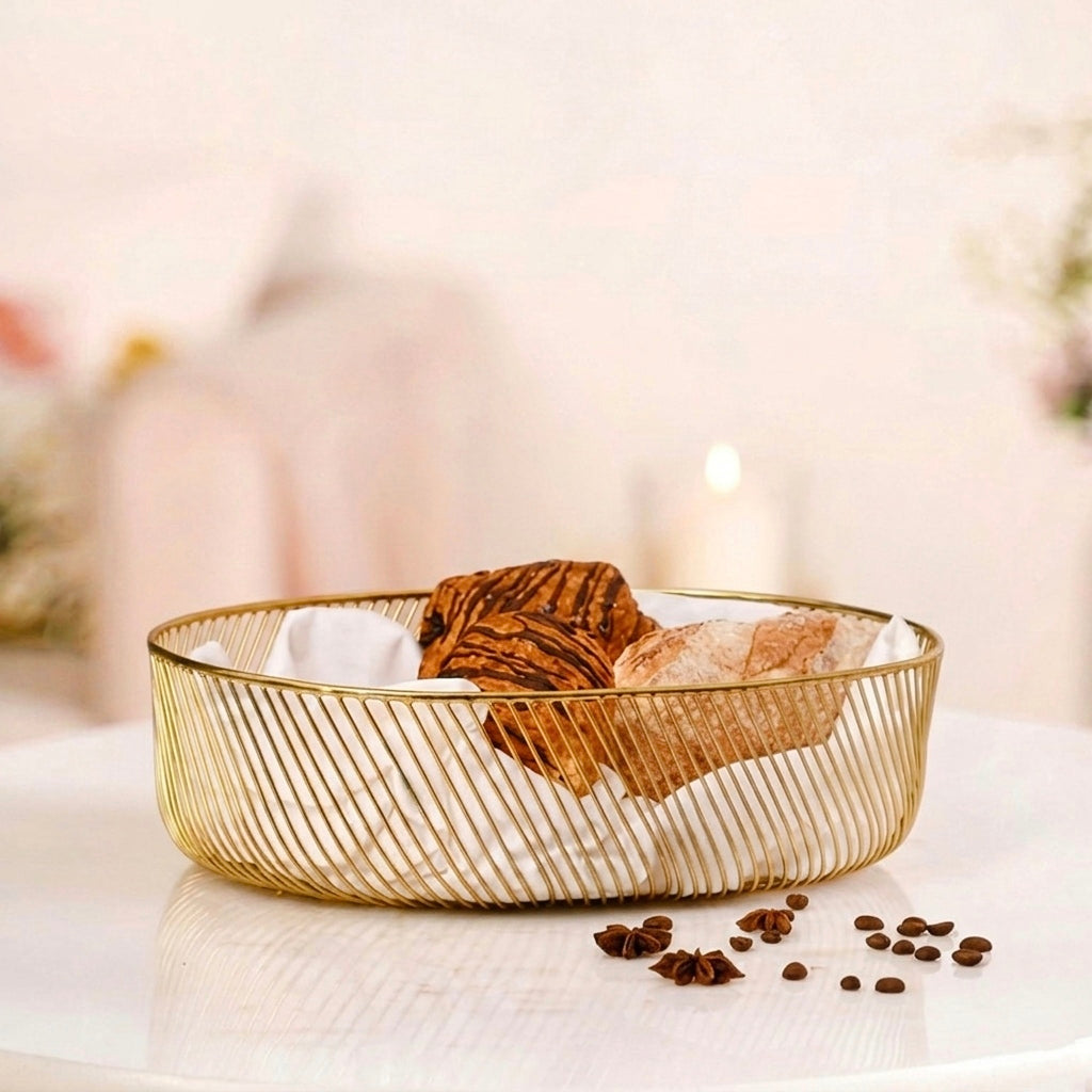 A modern gold wire decorative metal basket filled with pastries and a white cloth liner, sitting on a white marble surface with a solid blurred background.