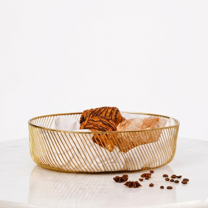 A modern gold wire decorative metal basket filled with pastries and a white cloth liner, sitting on a white marble surface with a solid white background.