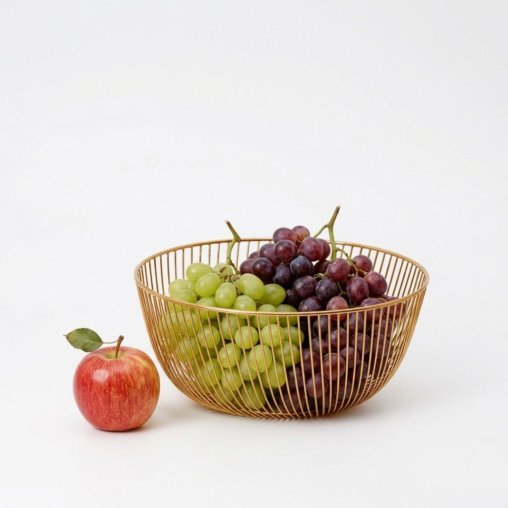 Sleek 10x10 inch gold metal wire basket on a solid white surface, styled as a modern minimalist fruit bowl containing green grapes and a red apple.