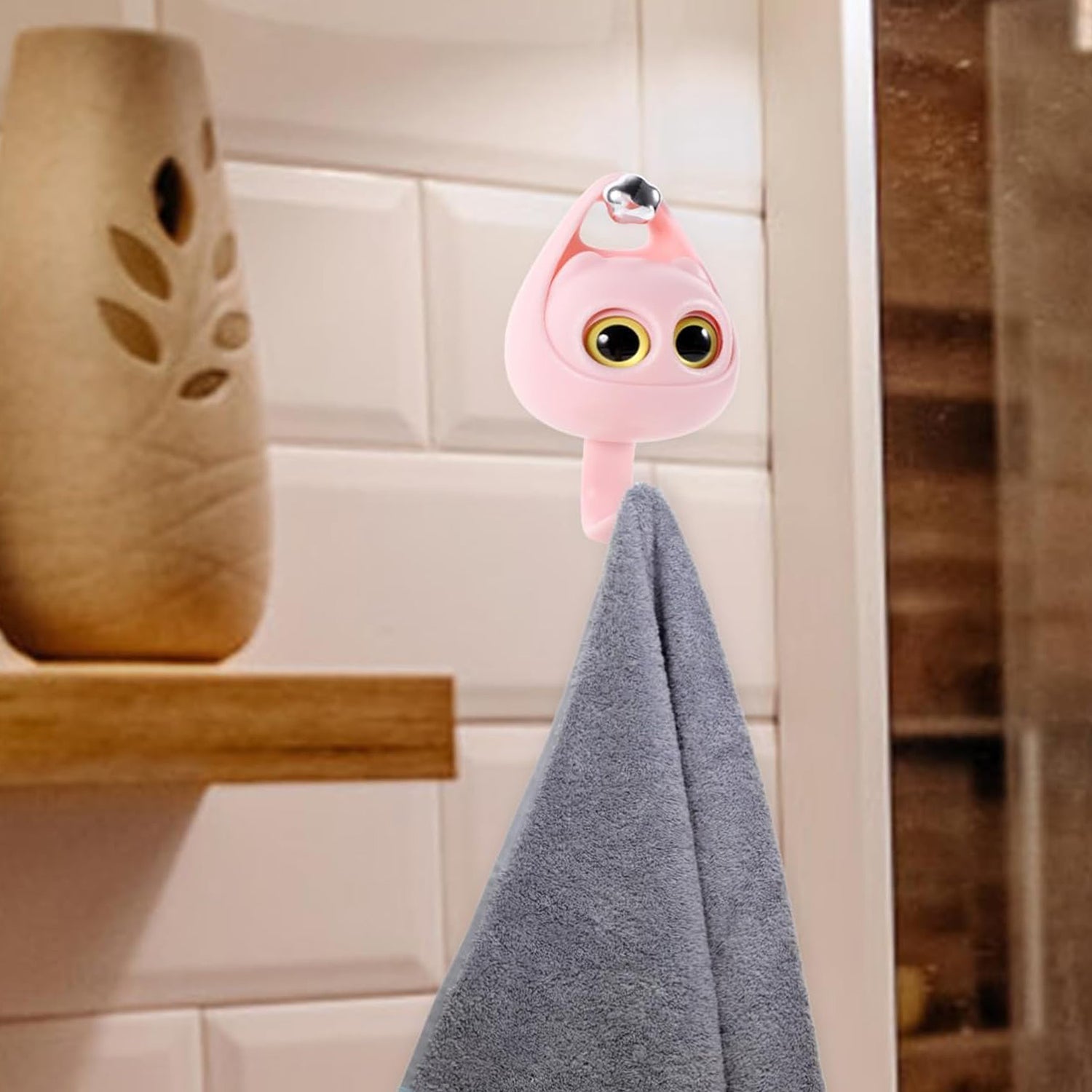 Decorative pink cat wall hook hanging a grey hand towel in a modern tiled bathroom setting